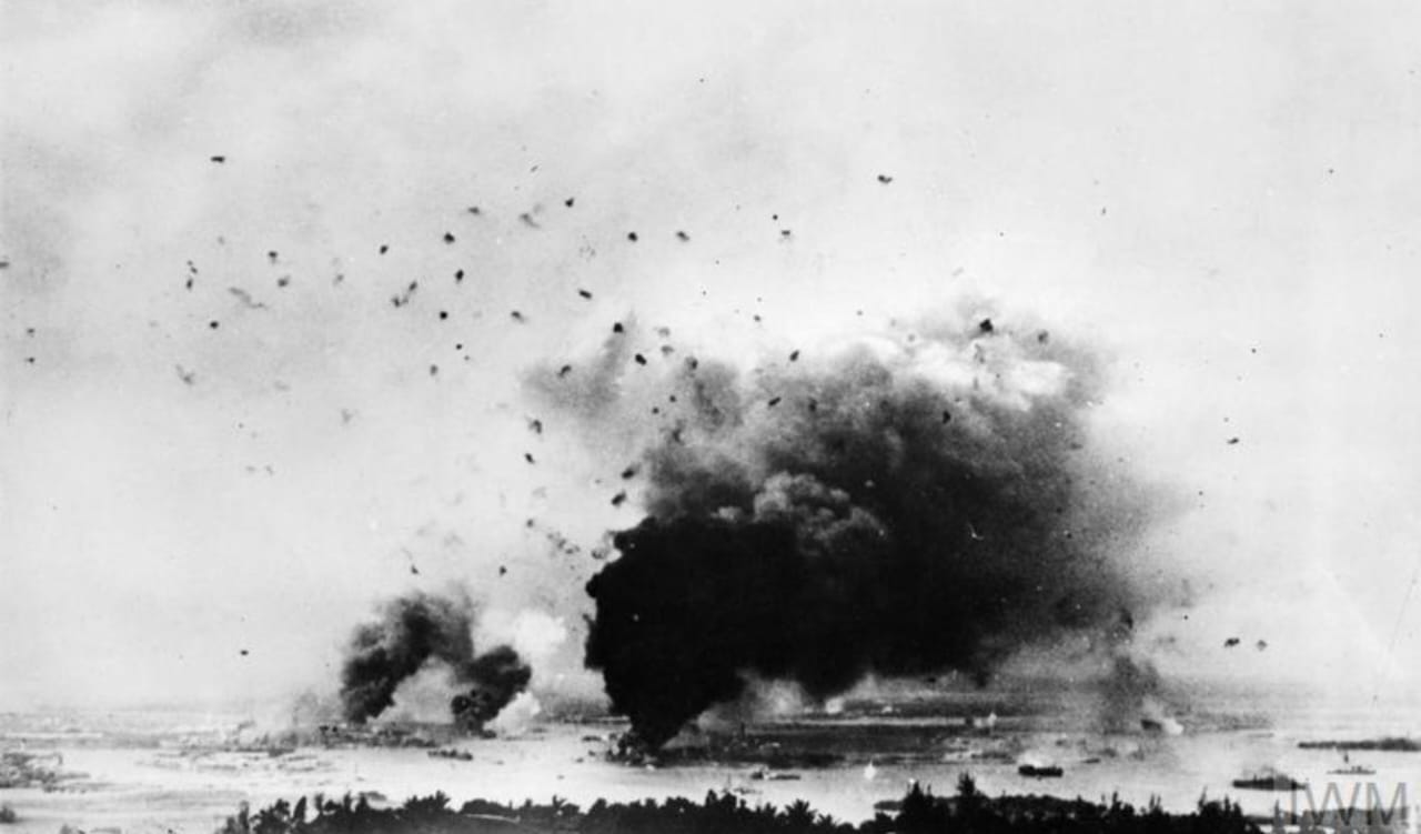 Pemandangan serangan di Pearl Harbour dilihat dari Pearl City. Asap mengepul dan langit dipenuhi puing-puing setelah ledakan di kapal USS Arizona. (Sumber: Imperial War Museums)